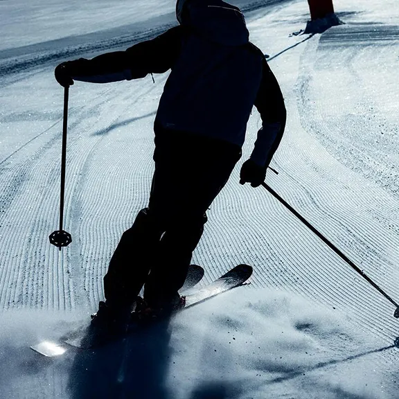Silhouette eines Skifahrers auf frisch präparierter, gerillter Piste im Gegenlicht.
